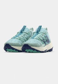 Chaussures de sport bleu clair avec tiges en mesh, détails texturés et embout renforcé. Semelle extérieure bleu foncé contrastante avec crampons multidirectionnels.