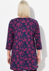 Tmavě modrá tunika s růžovým květinovým vzorem, 3/4 rukávy a zaoblený lem. Lehká tkanina s hladkou strukturou.