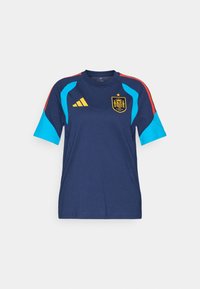 Ναυτικό μπλε ποδόσφαιρο φανέλα της Ισπανίας με ανοιχτό μπλε και κόκκινες λεπτομέρειες, λογότυπο Adidas και εθνόσημο της ισπανικής εθνικής ομάδας μπροστά.