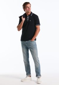 Marineblauwe polo met witte accenten, korte mouwen en een zak. Draagt met lichtblauwe jeans en witte sneakers. Minimalistisch ontwerp.