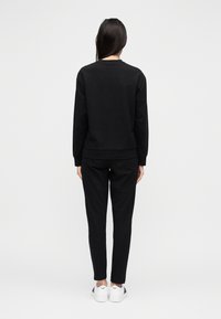 Μαύρο φούτερ και αντίστοιχο παντελόνι από μαλακό ύφασμα, με άνετη εφαρμογή και ριμπ μανσέτες. Συνδυασμένα με λευκά αθλητικά παπούτσια.