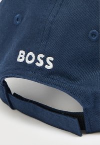 Cappellino blu navy in cotone con cinturino regolabile. Presenta la scritta "BOSS" ricamata in bianco sul davanti e un motivo a trama.