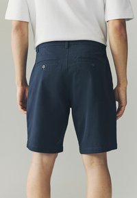 Marineblaue Shorts aus einem leichten Stoff; mit zwei Gesäßtaschen mit Knöpfen und einer flachen Vorderseite, designed für einen lässigen Schnitt.