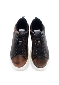 Hnedé kožené tenisky s čiernymi akcentami, šnurovací dizajn, zaoblená špička a biela gumová podrážka. Má textúrovaný povrch a logo na jazyku.