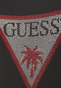 T-shirt noir avec un grand logo orné de strass rouges et blancs, représentant un palmier à l'intérieur d'un triangle.