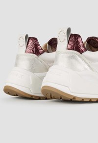 Sneakers bianche con accenti in argento metallizzato e bordeaux, caratterizzati da pelle testurizzata e una suola spessa in gomma. Logo del marchio sulla linguetta del tallone.