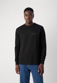 Černé tričko s dlouhým rukávem z bavlny, kulatý výstřih, s jemně embosovaným logem na hrudi a žebrovanými manžetami. Klasický střih.