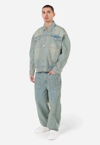 Svetlo modra denim jakna z dvema prsnikoma, v kombinaciji z ujemajočimi se svetlo modrimi širokimi hlačami, ki imajo edinstvene detajle šivanja žepov.