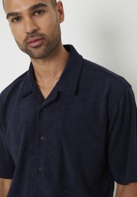 Camicia corta in cotone navy con colletto rilassato e una texture sottile, dotata di bottoni lungo la placca frontale.