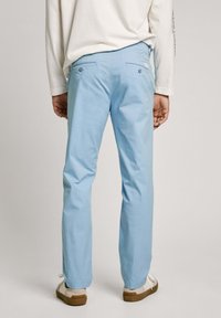 Gai zila kokvilnas bikses ar taisnu kāju, kurām ir divas aizmugures kabatas un izsmalcināta šuvju apdare, apvienotas ar gaišiem sporta apaviem.