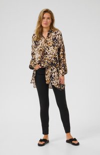Leopard print blouse with long sleeves and button closure, made of lightweight fabric. Paired with black skinny jeans and black sandals.