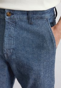 Jeans w średnim niebieskim odcieniu z zapięciem na guzik, dwoma bocznymi kieszeniami oraz prostymi nogawkami, prezentujące subtelną teksturę.