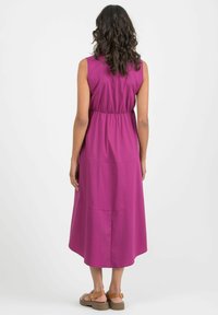 Fuchsia ärmelloses Kleid mit gerafftem Taillenbereich, knielang, glatter Textur und ausgestelltem Saum. Kombiniert mit braunen Riemchensandalen.