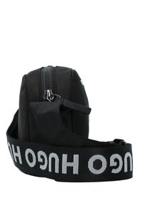 Borsa nera in nylon di forma rettangolare, chiusura con zip e tracolla regolabile con logo "HUGO" in bianco. Superficie testurizzata con design minimal.