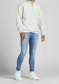 Light gray zip-up sweatshirt with ribbed cuffs, paired with fitted light blue jeans and white high-top sneakers. Simple and modern design.
