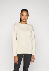 Beige huppari, jossa on pyöreä kaula-aukko ja pitkät hihat. Hupparissa on pieni valkoinen logo rinnassa sekä joustavat hihansuut ja helma.