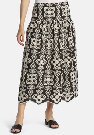 Black midi skirt with white floral lace embroidery, scalloped hem, worn with black open-toe slide sandals and a white top.
