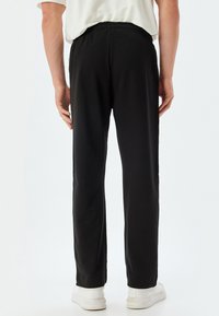 Pantalones de algodón negros con una cinturilla elástica. Corte recto con textura suave, sin bolsillos visibles ni patrones.