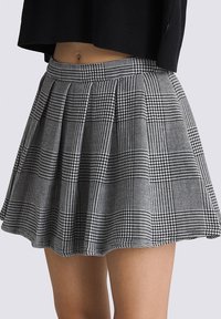 Falda plisada de cuadros en blanco y negro con una cinturilla ajustada, hasta la rodilla, hecha de un tejido texturizado que presenta patrones de pata de gallo y cuadros.