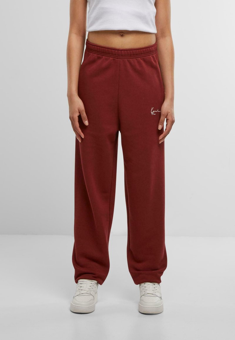 Burgundijas krāsas plašas bikses no mīksta auduma ar elastīgu jostasvietu un smalku izšūtu logotipu uz kreisā augšstilba.