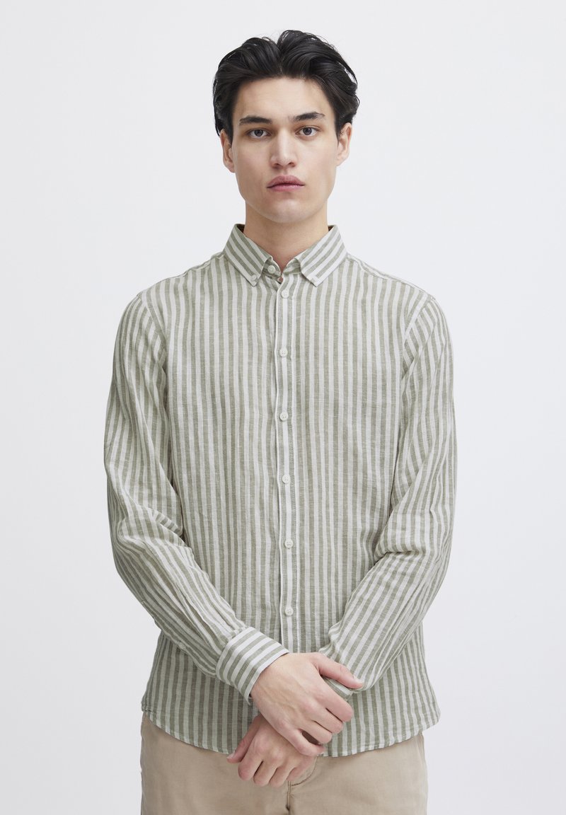 Camisa de botones a rayas verdes y blancas con cuello puntiagudo, mangas largas y textura ligera, que presenta un dobladillo recto y puños abotonados.