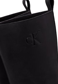Čierne kožené členkové topánky s texturovaným povrchom, embosovaným logom a dvojitými pútkami pre jednoduché obúvanie. Hladký, elegantný dizajn.