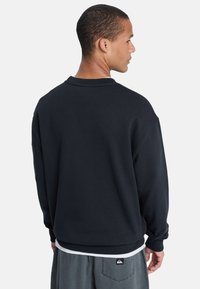 Zwarte sweatshirt met een ontspannen pasvorm, ronde kraag en lange mouwen. Zachte stof, effen kleur, met een logopatch nabij de zoom.