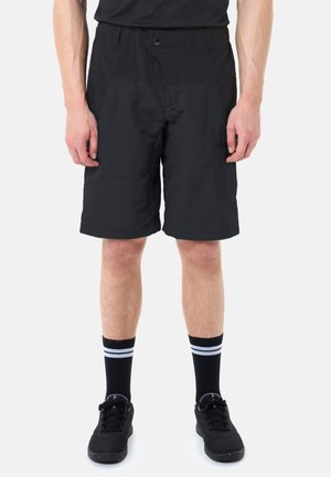 Mann trägt schwarze knielange Shorts mit Seitentaschen, schwarze Turnschuhe und schwarze Socken mit zwei weißen Streifen, steht vor weißem Hintergrund.