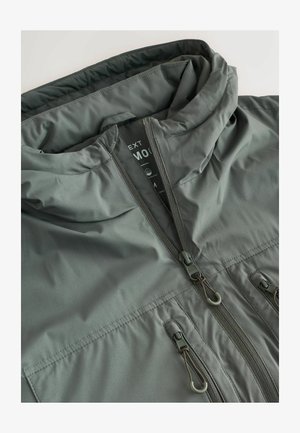 Veste imperméable grise avec capuche, dotée d'un zip complet, de deux poches avant et de réglages par cordon. Texture lisse et finition mate.
