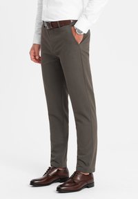 Tummanharmaat, slim fit -housut, joissa on sileä pinta. Edessä on taskut ja ruskea vyö. Yhdistetty ruskeisiin nahkakenkiin.