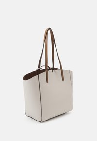 Sac fourre-tout rectangulaire beige avec des doubles bretelles marron et des détails noirs sur les bords, présenté sur un fond uni clair.