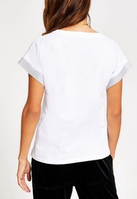 Bílý krátký rukáv s texturovaným šedým lemem na rukávech, se jednoduchým designem a měkkým materiálem, z pohledu zezadu.