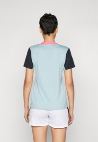 Camiseta deportiva de manga corta en azul claro con mangas negras y un cuello rosa, confeccionada en tejido transpirable, combinada con pantalones cortos blancos.