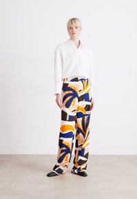 White button-up shirt paired with wide-legged trousers featuring a colorful abstract pattern in orange, blue, brown, and cream. Black shoes.