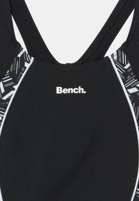 Haut de maillot de bain noir avec panneau latéral à motif, fabriqué en tissu lisse. Présente un design dos nageur et un logo "Bench." blanc à l'avant.