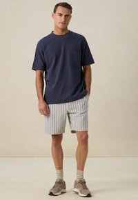 T-shirt en coton bleu marine avec une poche, associé à un short à rayures blanches et multicolores, complété par des baskets beiges et des chaussettes.