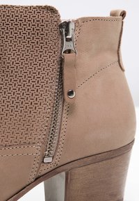 Tan nilon korkunç ayakkabı, dokuma doku paneli ile birlikte. Metal donanımlı yan fermuar ve ahşap topuk ile dikkat çekiyor. Pürüzsüz deri yüzeye sahip.