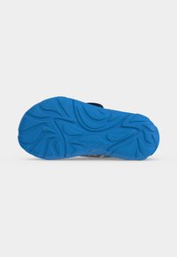 Semelle en caoutchouc bleue d'une sandale avec des rainures décoratives et un logo "KangaRoos" visible en dessous.
