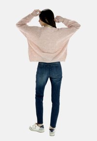 Rosa gerippter Pullover mit weiten Ärmeln, kombiniert mit dunkelblauen Skinny-Jeans und weißen Sneakers mit silbernem Sternmotiv.