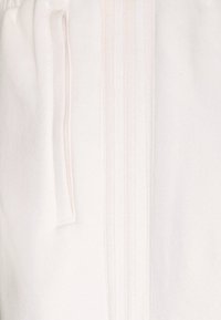 Vita joggingsbyxor gjorda av mjukt tyg, med subtila vertikala ränder och sidofickdetalj. Slät textur med avslappnad passform.