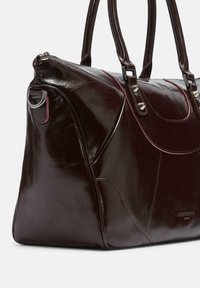 Ciemnobordowa skórzana torebka o błyszczącym wykończeniu. Posiada podwójne uchwyty, srebrne okucia oraz subtelne akcenty w postaci przeszyć. Elementy o zaokrąglonym kształcie.
