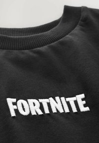 Sort sweatshirt med en ribbet halsudskæring og hvidt broderet "FORTNITE"-logo på forsiden. Blødt stof med en glat tekstur.