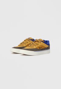 Sneakers din suede maro și galben cu accente albastre, șireturi plate și tălpi din cauciuc alb, având un logo subtil al brandului pe lateral.