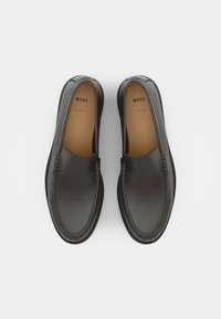 Paire de mocassins noirs en cuir sans lacets avec bouts arrondis et semelles intérieures beige marquées du texte BOSS, vus de dessus sur un fond clair.