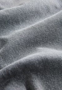 Grauer Denim-Stoff mit feiner Textur und gewebtem Muster, der sanfte Falten und ein leicht gebürstetes Aussehen zeigt.