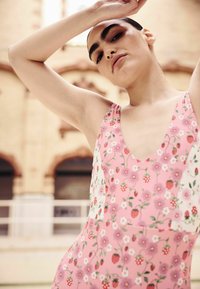 Pink floral dress featuring a deep V-neck, with a pattern of strawberries and flowers, made of smooth fabric. Light background details.