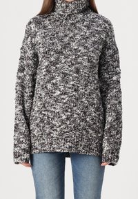 Gestrickter Rollkragenpullover in Schwarz und Weiß, mit einem strukturierten, gesprenkelten Muster und überschnittenen Schultern für eine lockere Passform.