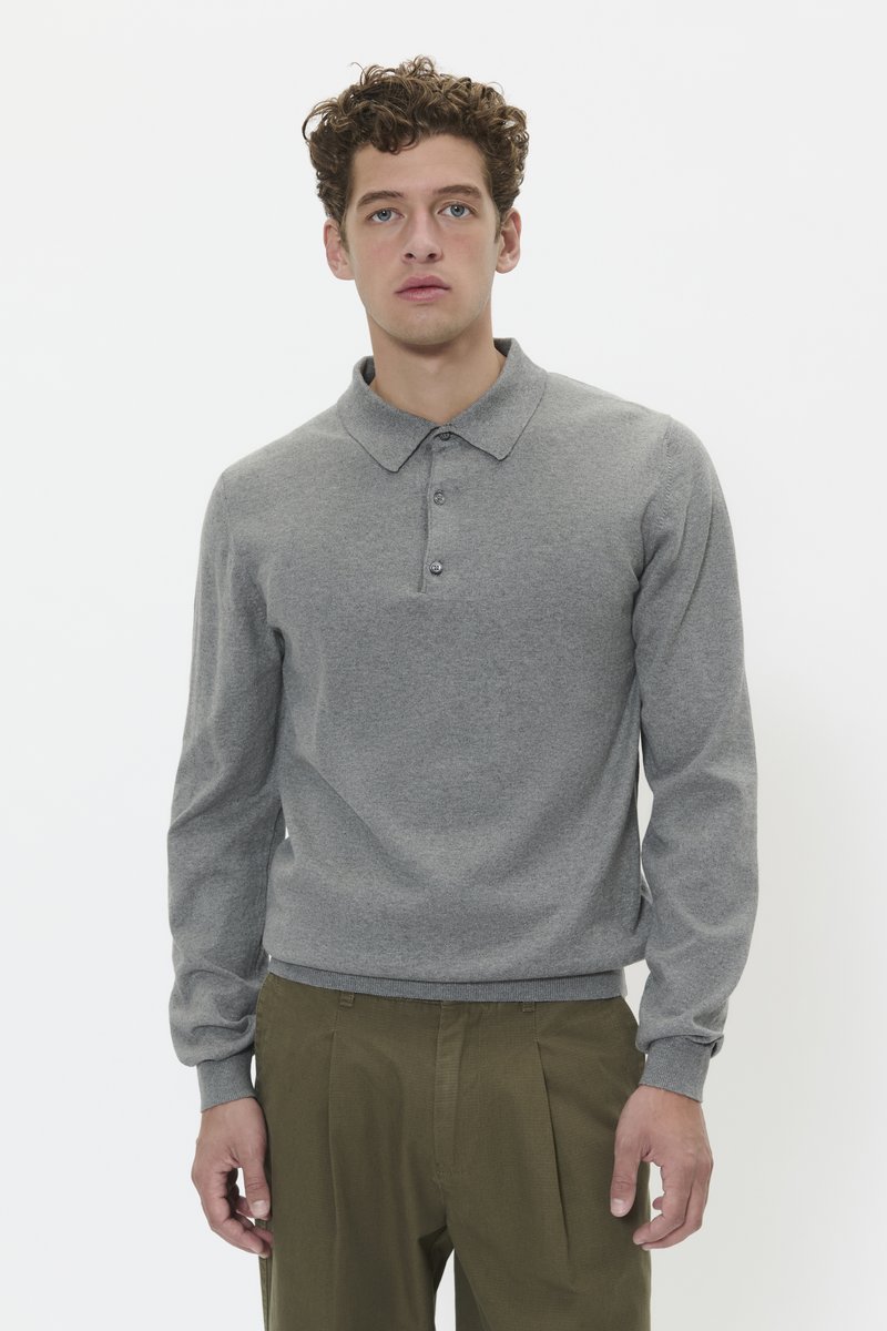 Polo grigio a maniche lunghe con colletto, tre bottoni e polsini a coste. Il tessuto sembra morbido con una texture liscia, indossato con pantaloni verde oliva.