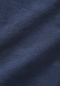 Tissu bleu foncé texturé avec un motif de losanges tissé subtil et des plis visibles créant des ombres douces.