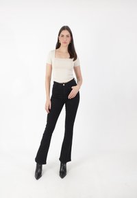 Haut crème à manches courtes avec un décolleté carré, assorti à un jean noir évasé et des escarpins noirs à bout pointu. Texture lisse, design ajusté.